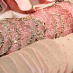 Mortadella su un tagliere con verdure fresche, in un articolo sull'ipertensione e la dieta.