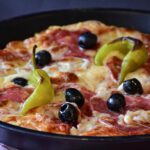 Pizza in teglia con bordo basso e ingredienti freschi, evidenziando problemi di lievitazione.